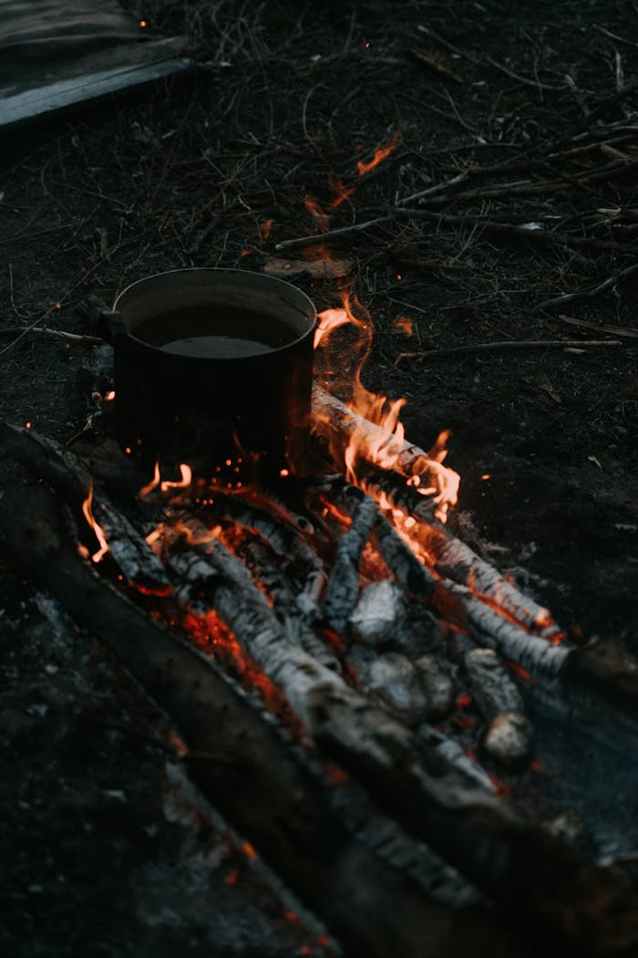 A rustic scene featuring a pot on an open fire with burning embers, ideal for camping themes.